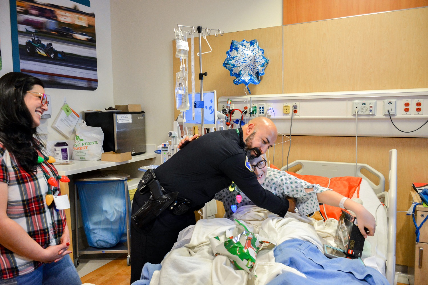 A police officer hugging a child in a hospital bed, both are smiling